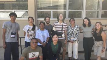 Group photo of adults smiling outdoors in front of building windows