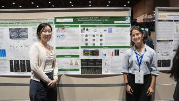 Two women smiling beside a research poster at a conference